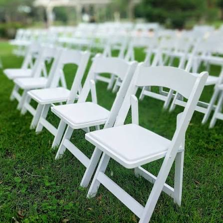 Rows of white resin padded folding chairs set up outdoors for a ceremony