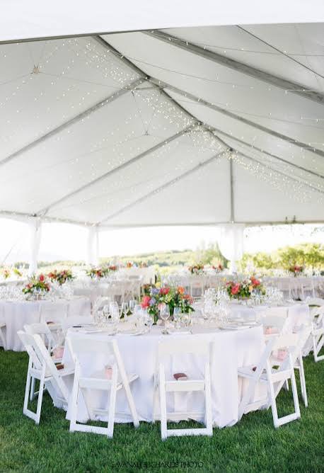 Tented reception with white folding chairs and round tables